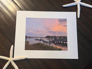 Framed photograph of a harbor scene with a sunset, placed on a wooden surface with starfish.
