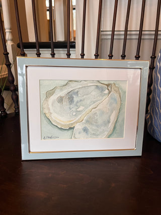 Framed artwork watercolor painting in aquas of an oyster shell on a wooden surface.