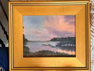 Framed painting of a coastal landscape with a river and pink sky.