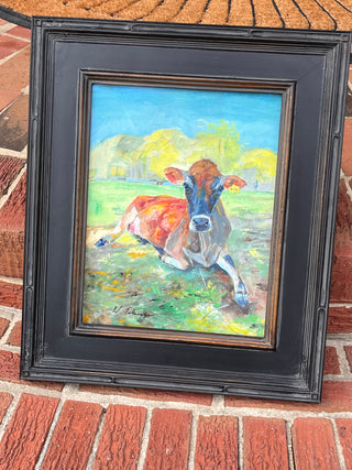 Framed painting of a cow in a field on a brick surface